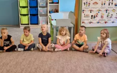 Przedszkolaki sziedzące na dywanie w czasie czytanej bajki