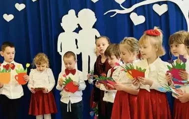 Dzieci stoją z kolorowymi laurkami dla babć i dziadk&oacute;w