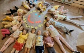 Dzieci z Grupy II leżąc na podłodze tworzą koło, w środku kt&oacute;rego znajduje się uśmiech.