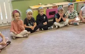 Przedszkolaki siedzące na dywanie i słuchające czytanej bajki