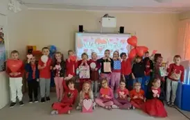 Grupa Starszak&oacute;w trzyma balonowe i papierowe serca, prezenty na tle napisu "Walentynki"