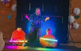 Chłopiec i dziewczynka siedzą na scenie ubrani w kosmiczne/powietrzne kule. Trzymają w ręku ledowe, kolorowe lampy.