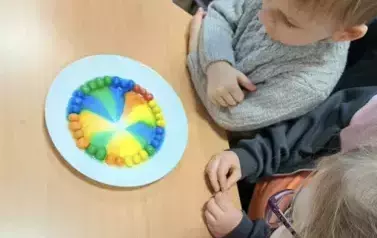 Tęcza na talerzu powstała z cukierk&oacute;w zanurzonych w widzie
